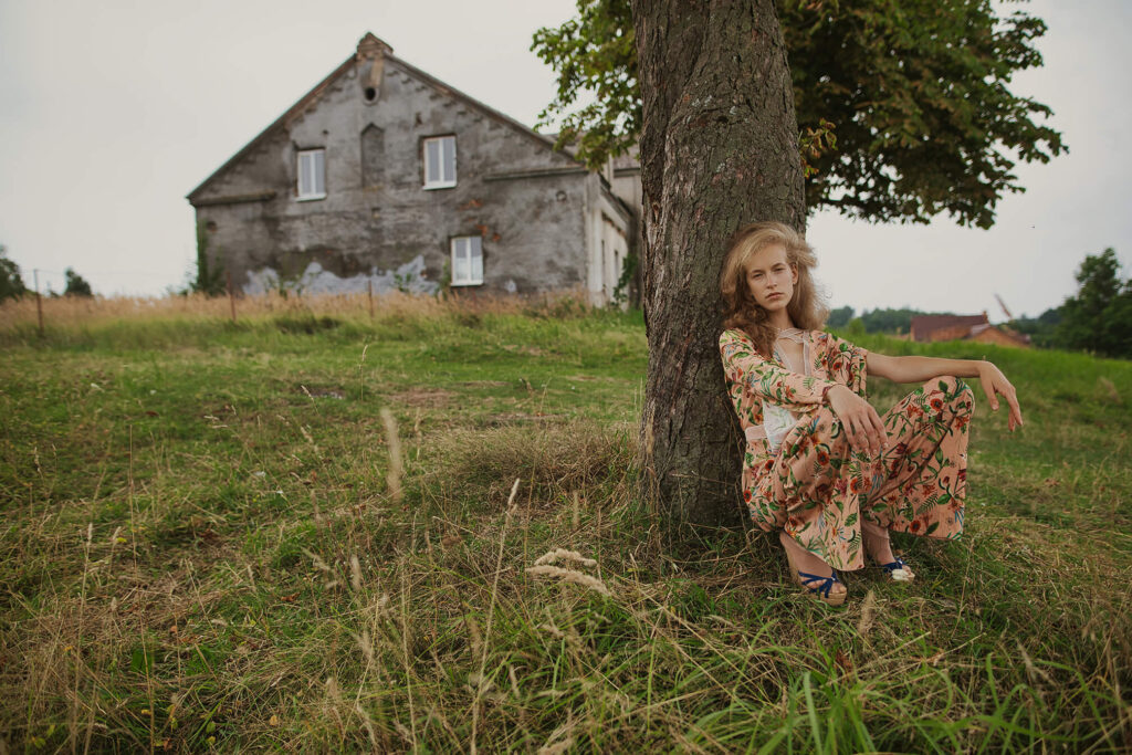 Девушка, сидящая под деревом возле старого дома